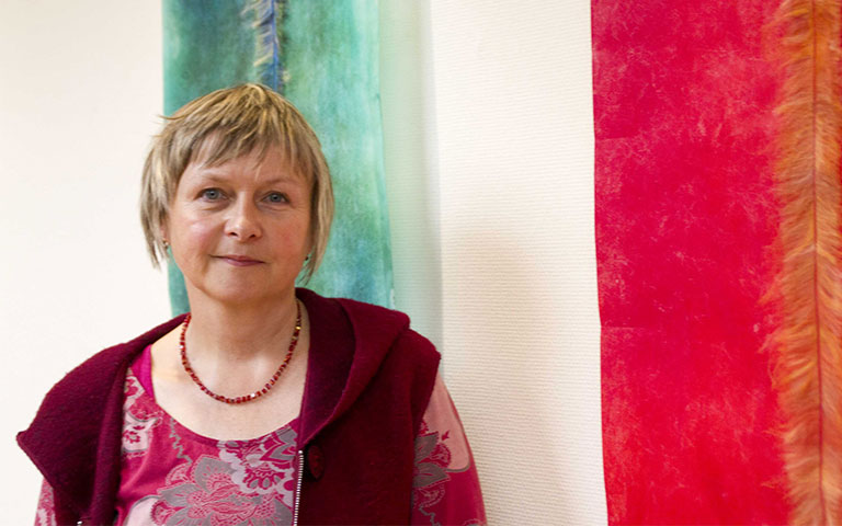 Bild Nora Grawitter mit textilem Kunstwerk im Hintergrund 